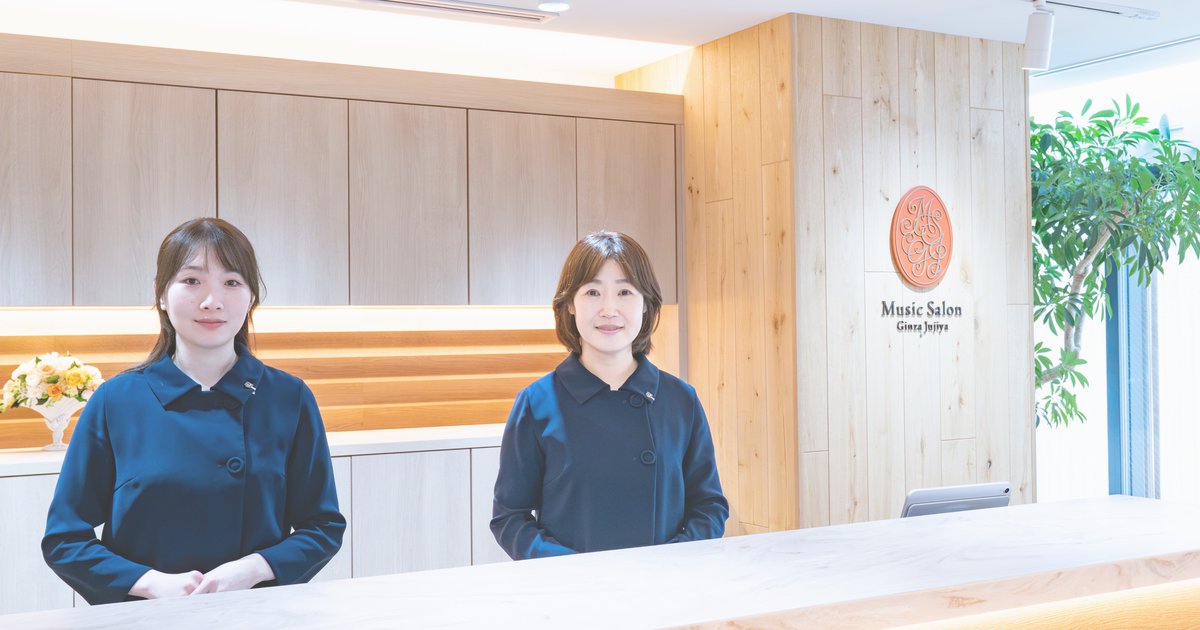 ミュージックサロン銀座十字屋の受付カウンターに立つ、制服姿のスタッフ2名