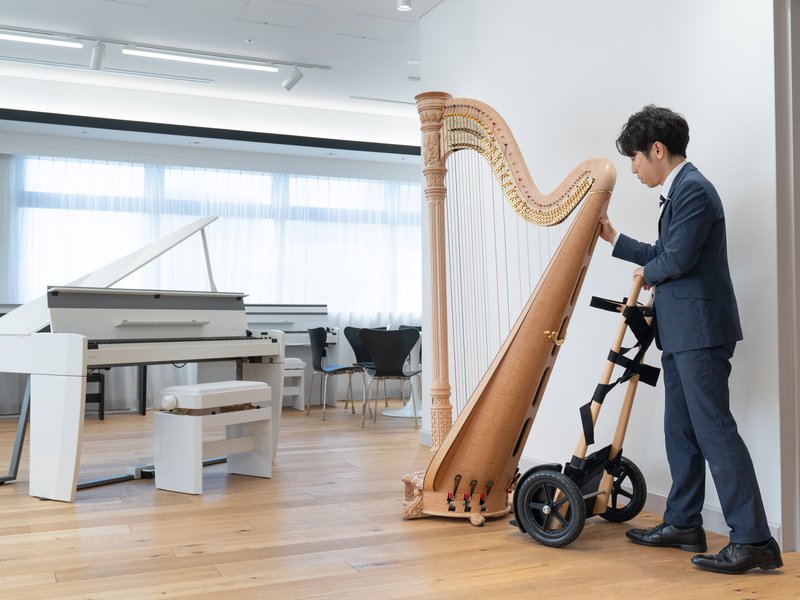 台車に固定したグランドハープを、ピアノの置かれた部屋へ搬入する銀座十字屋のスタッフ