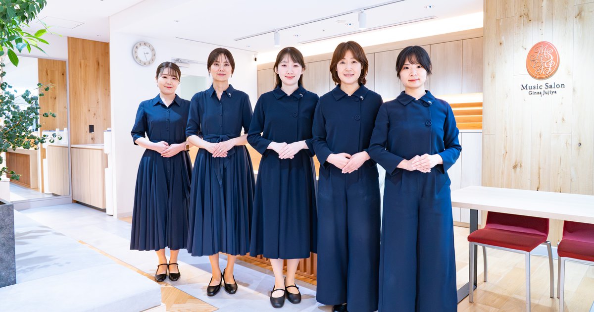 ミュージックサロン銀座十字屋の受付前に並ぶ、制服姿のスタッフ5名