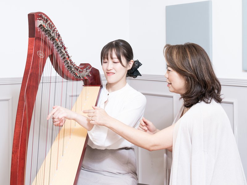 レバーハープに向かう受講者の手の形を、横に立った講師が指導する様子